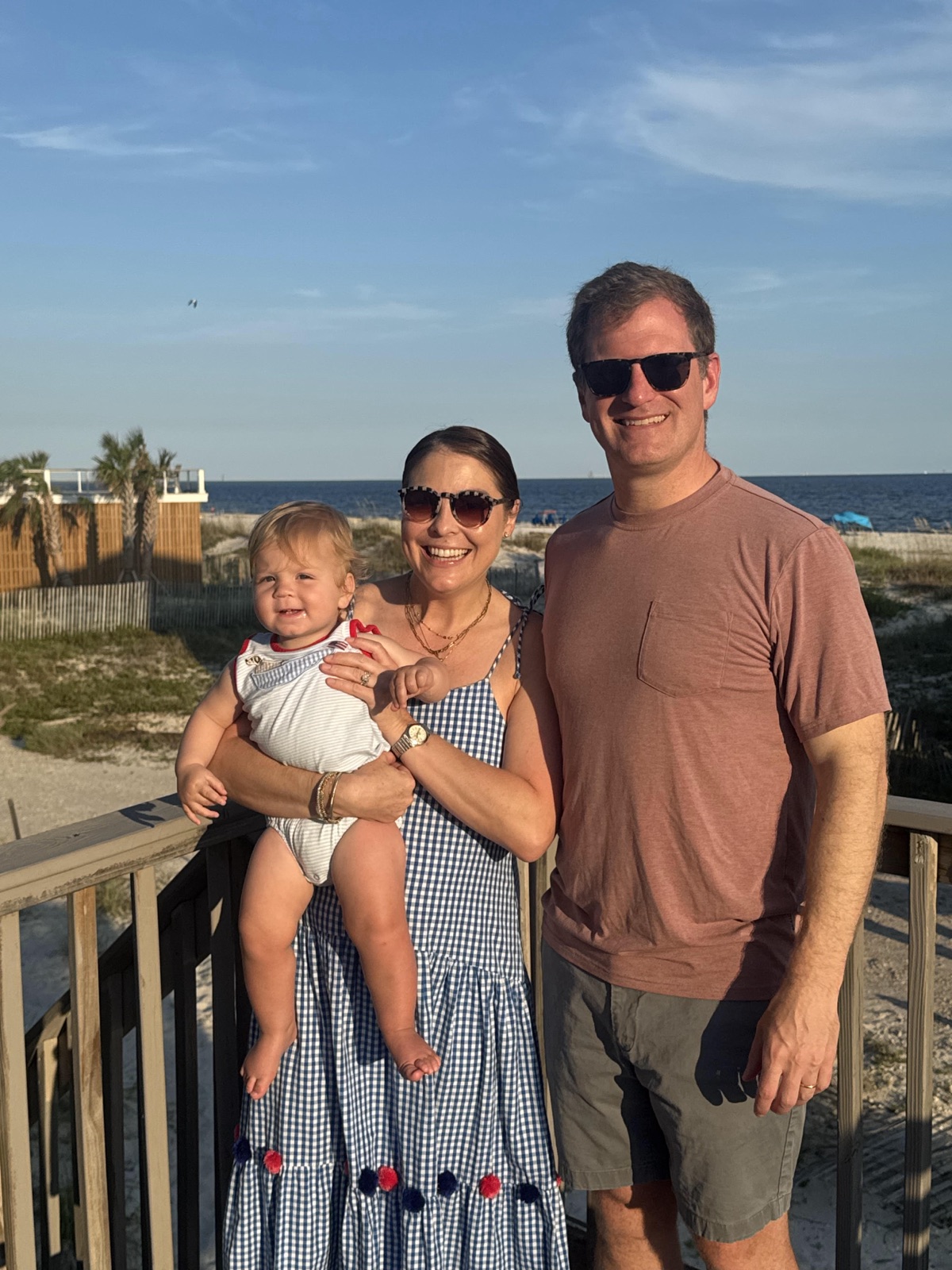 The Frost family on a deck overlooking the beach, holding a smiling baby.